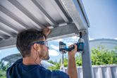 A person wearing safety equipment uses an impact wrench on a metal structure.