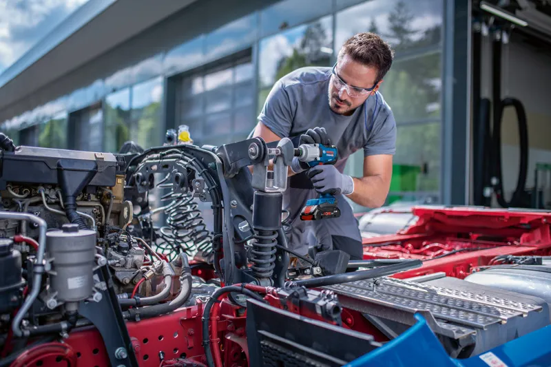 GDS 18V-450 HC A person wearing safety equipment uses a cordless impact wrench on a vehicle chassis.