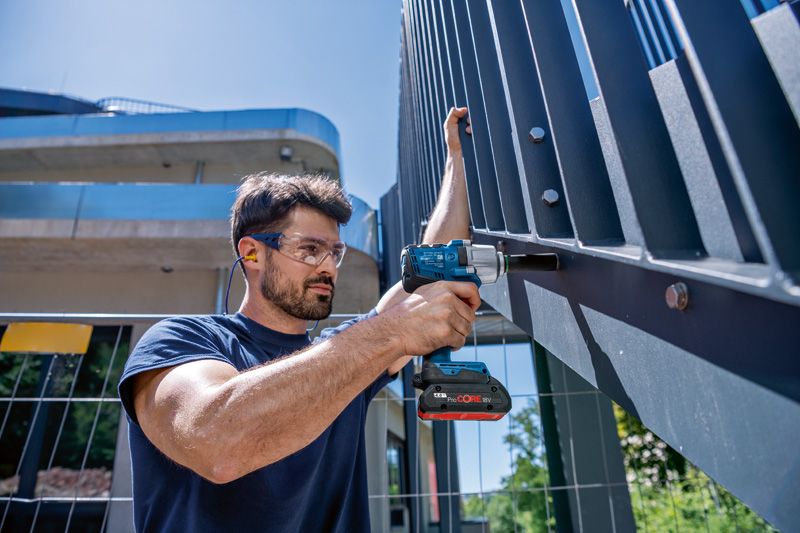 GDS 18V-450 HC A person wearing safety equipment uses a cordless impact wrench on a metal fence.