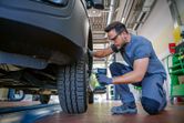 A person wearing safety equipment uses a cordless impact wrench to tighten a car wheel bolt.