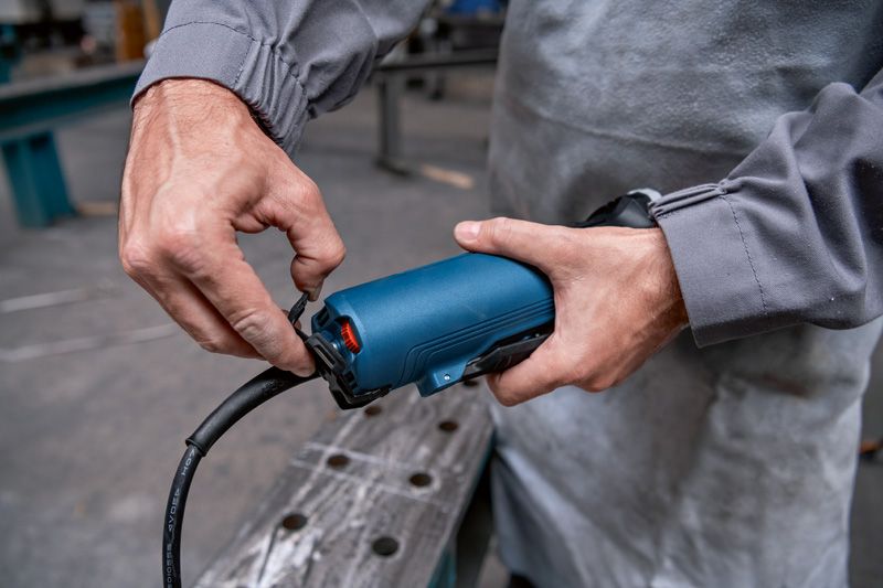 Person in workwear connecting a power cord to a blue handheld tool.