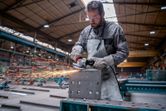 A person wearing safety equipment uses an angle grinder to cut a metal box, producing sparks.
