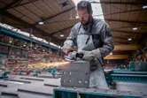 A person wearing safety equipment grinds a metal block with an angle grinder, producing sparks.