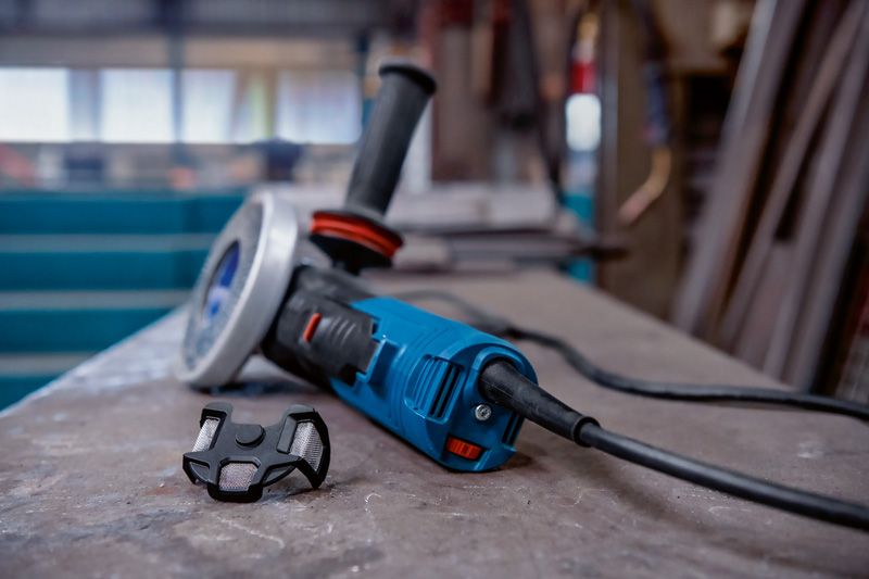 Electric angle grinder resting on a workbench beside a small dust filter.