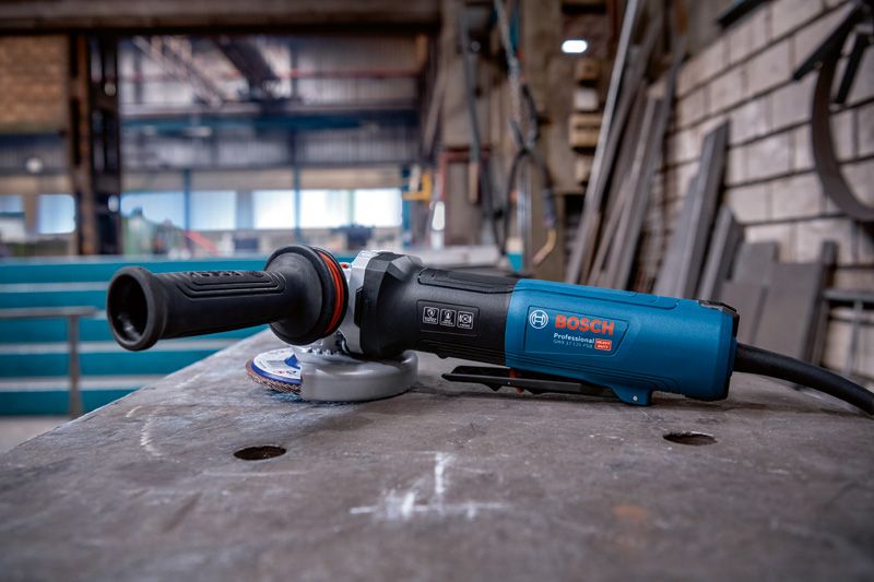 Angle grinder with X-LOCK rests on a workbench in a metal workshop.
