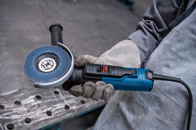 A person wearing safety equipment holds an angle grinder with flap disc.