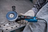 A person wearing safety equipment holds an angle grinder with flap disc.