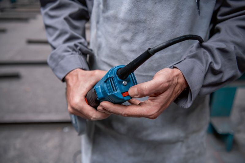 A person wearing safety equipment holds and inspects an angle grinder power tool.