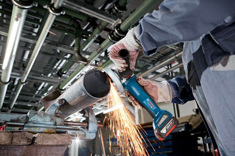 GWS 18V-10 P A person wearing safety equipment grinds a metal pipe with a cordless angle grinder.