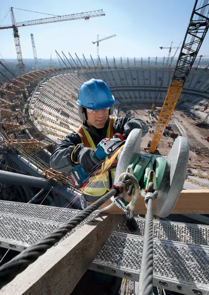 GWS 18V-10 P A person wearing safety equipment uses an angle grinder on a steel beam at a stadium construction site.