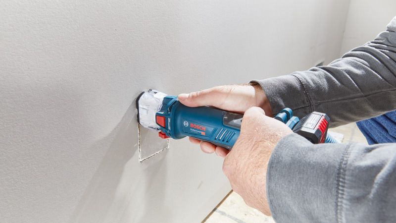 A person cuts a rectangular hole in drywall using a cordless drywall router.