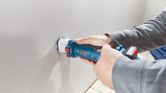A person cuts a rectangular hole in drywall using a cordless drywall router.