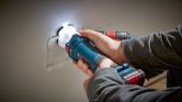 A person cuts a rectangular hole in drywall using a cordless drywall router.
