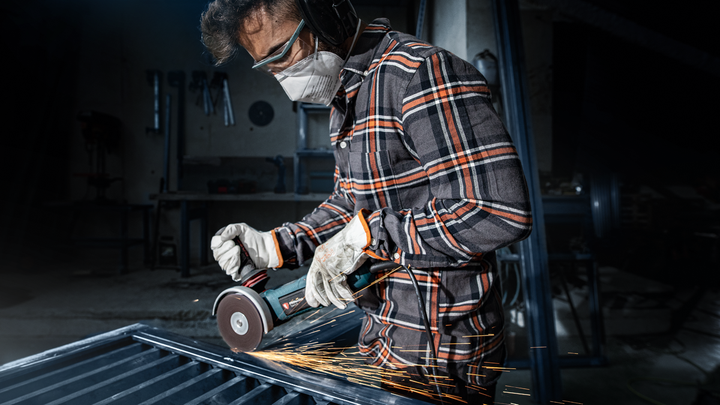 Person wearing safety equipment grinds metal, creating sparks.