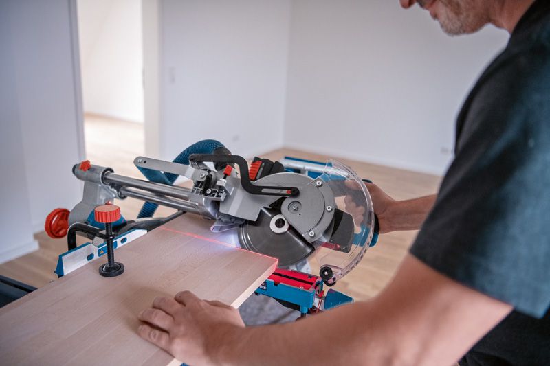A person cuts wood using a cordless mitre saw with a laser leveling tool.