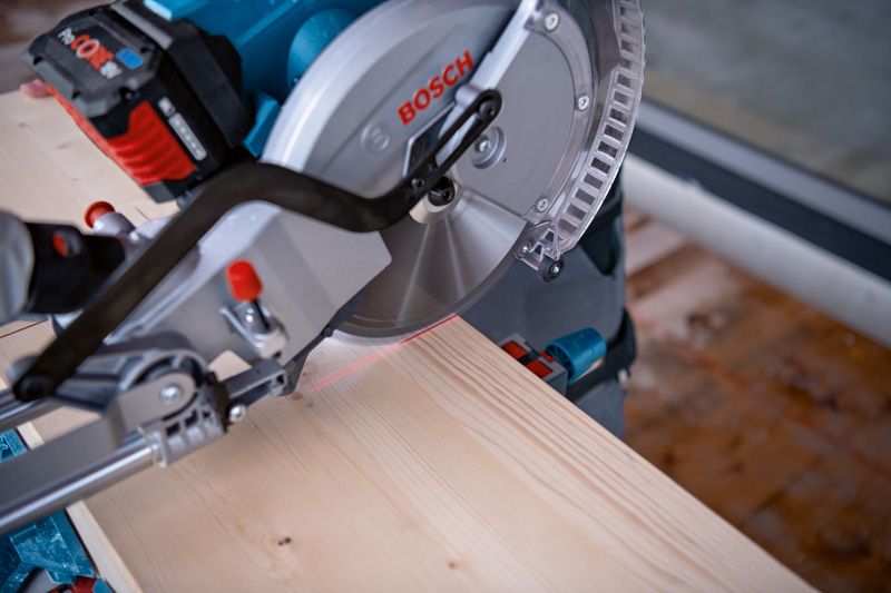 Cordless mitre saw cutting a wooden board with a laser leveling tool.