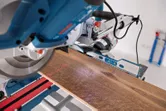 Mitre saw with a laser leveling tool cutting a wooden plank on a workbench.