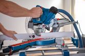 A person cuts a piece of trim with a mitre saw using a laser leveling tool.