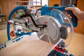 Person guiding a mitre saw to cut wood, dust extraction hose attached.