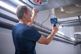 A person inspects inside an overhead duct using an inspection camera in a utility room.