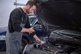 A person inspects a car engine using an inspection camera in a workshop.