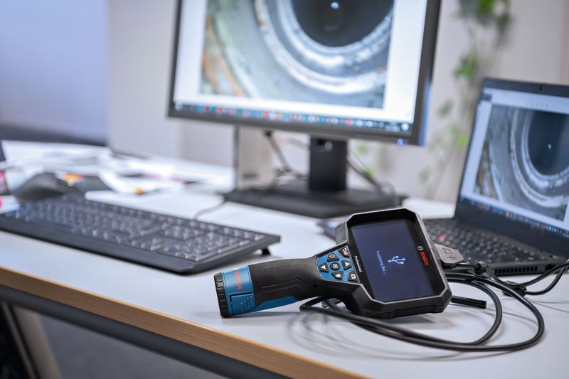 Inspection camera connected to a laptop on an office desk with pipe images on screens.