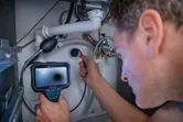 A person inspects pipes under a sink using an inspection camera.