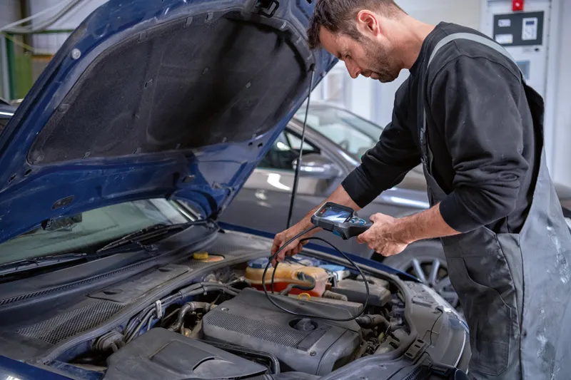 A person inspects a car engine using an inspection camera.