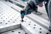 A person wearing safety equipment polishes a metal frame with a rotary grinder.