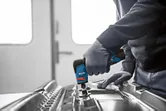 A person wearing safety equipment polishes metal with a rotary grinder.