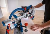 A person uses a cordless mitre saw to cut wood, guided by a laser leveling tool.