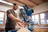 A person prepares to cut wood with a mitre saw in a workshop.