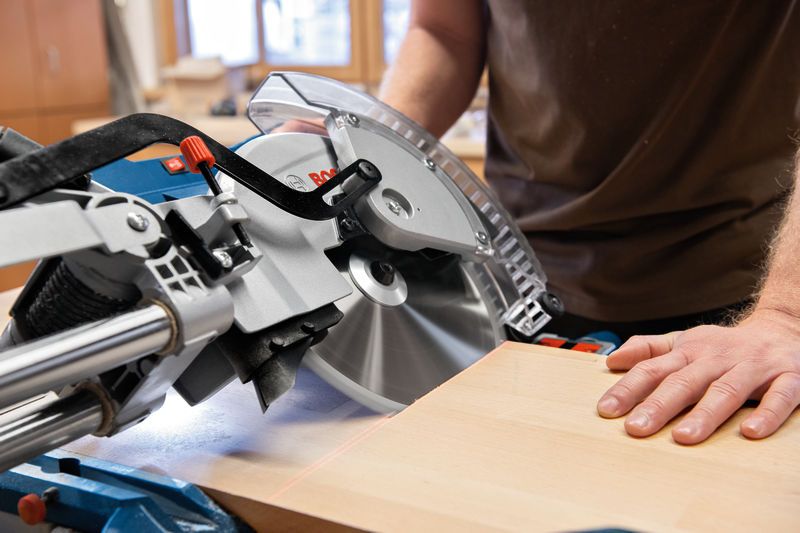 A person operates a mitre saw to cut wood in a workshop.