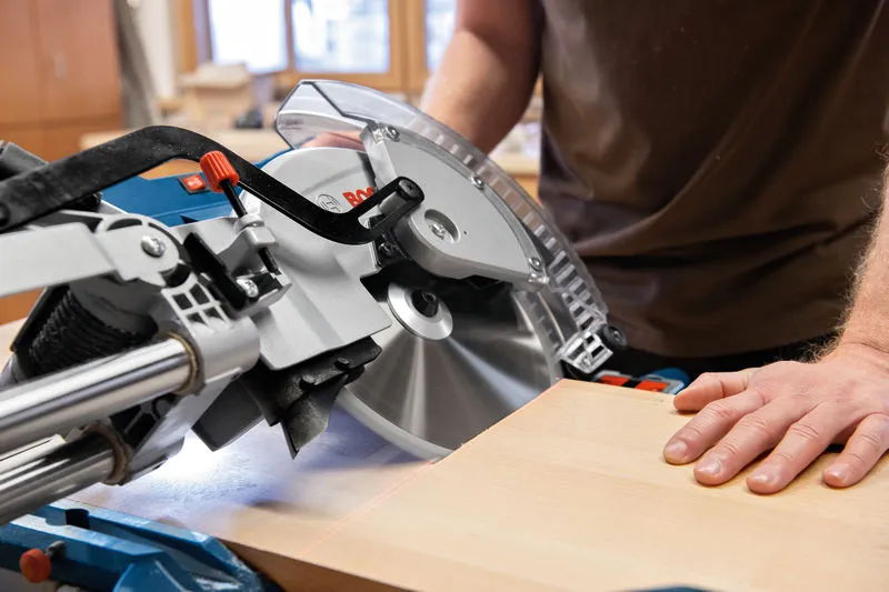 A person operates a mitre saw to cut wood in a workshop.