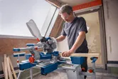 A person wearing safety equipment cuts wood with a cordless mitre saw.