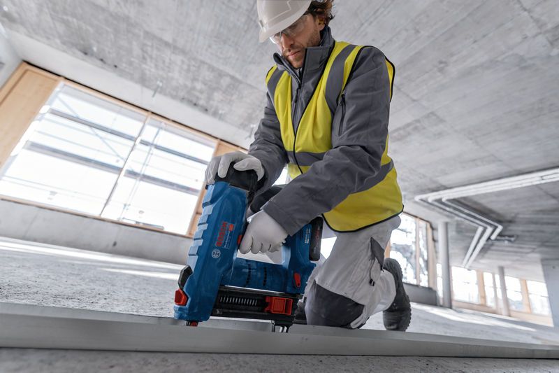 Person wearing safety equipment uses a power tool to fasten a metal frame on a construction site.