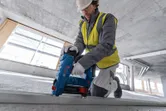 Person wearing safety equipment uses a power tool to fasten a metal frame on a construction site.