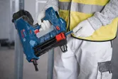 A person wearing safety equipment loads nails into a blue cordless concrete nailer.