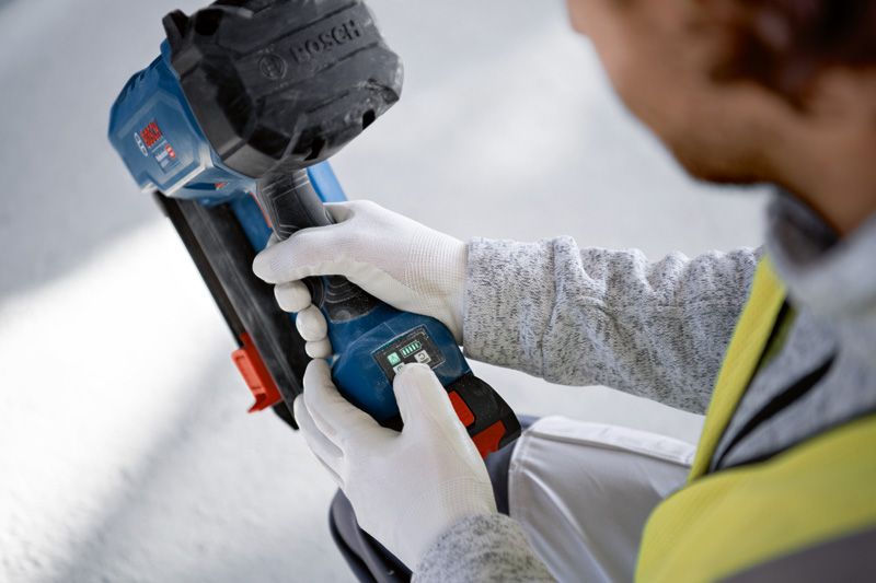 Person wearing safety equipment adjusts a cordless power tool on a construction site.