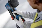 Person wearing safety equipment adjusts a cordless power tool on a construction site.