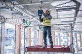 A person wearing safety equipment drills into a concrete ceiling on a construction site.