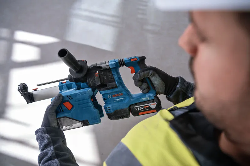 A person wearing safety equipment holds a cordless rotary hammer drill.