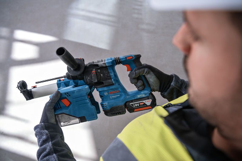 A person wearing safety equipment holds a cordless rotary hammer drill.
