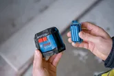 A person holds a laser leveling tool and a battery pack.