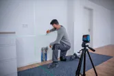 Person kneeling while marking a wall with guidance from a laser leveling tool.