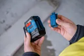 A person opens a battery compartment of a blue and black power tool.