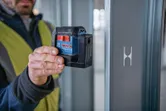A person wearing safety equipment uses a laser leveling tool against a metal beam.