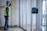 A person wearing safety equipment marks a wall using a laser leveling tool.