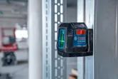 Laser leveling tool projecting green lines, attached to a metal frame in a construction area.