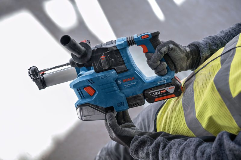 A person wearing safety equipment holds a cordless rotary hammer drill.